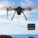 A black quadcopter drone flying over the ocean with rocks in the foreground, shown carrying a Newton-3 with Mechanical Fishing Release System. The background is a blue sky and sea.