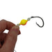 A close-up of a hand holding a fishing lure with a black hook, translucent white beads, and a bright yellow and orange gradient bead on a plain white background.