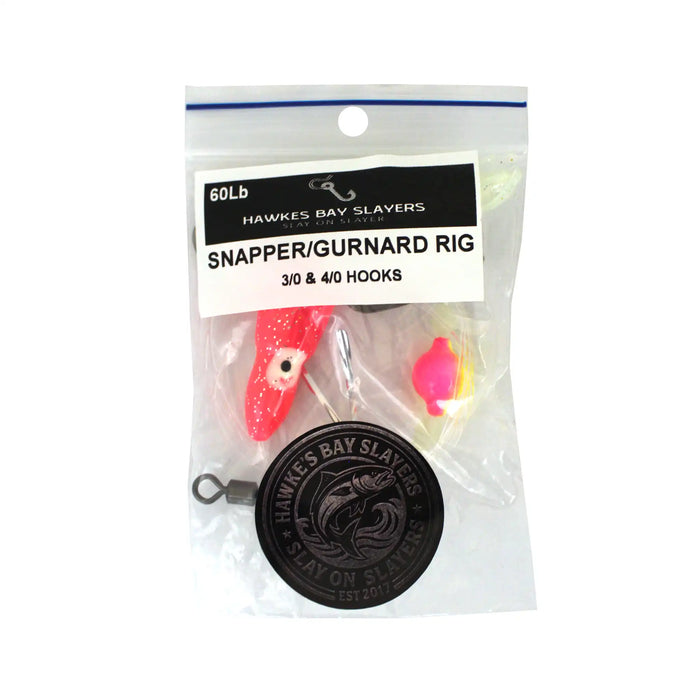 A packaged fishing rig labeled 'Hawkes Bay Slayers Snapper/Gurnard Rig' in a clear plastic bag with a printed header card. The rig includes a red and white lure, a bright pink and yellow bead, metal eye hooks, and a black circular branded weight or weighter.